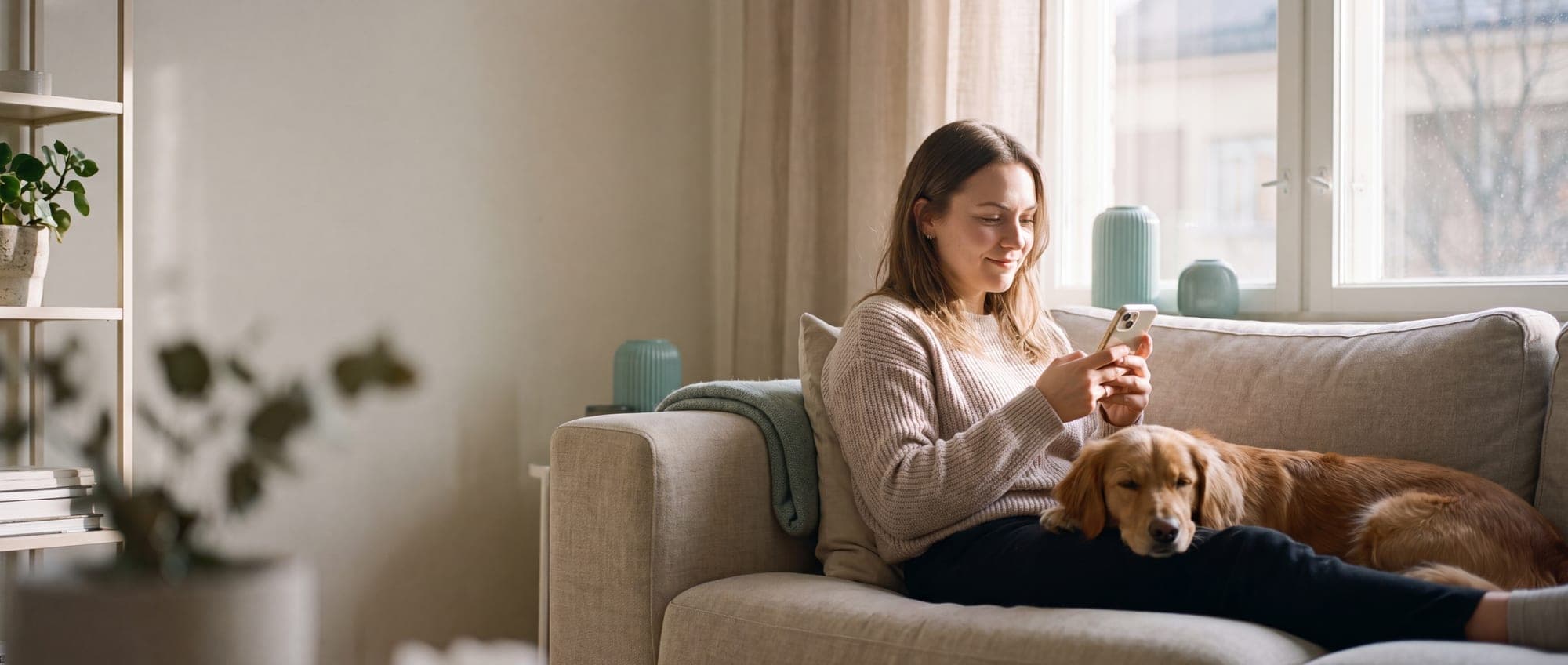 Una donna consulta lo smartphone sul divano mentre il suo cane riposa accanto a lei
